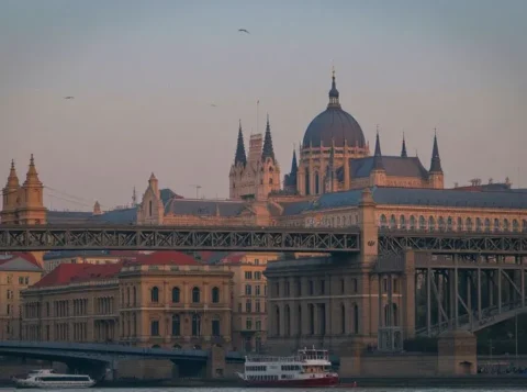 Scenic night view of Budapest’s Parliament Building lit up along the Danube River with Chain Bridge glowing under the evening sky.