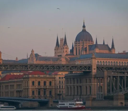 Scenic night view of Budapest’s Parliament Building lit up along the Danube River with Chain Bridge glowing under the evening sky.