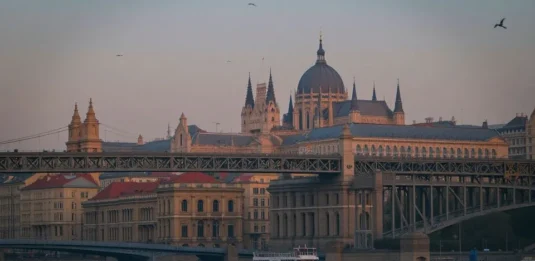 Scenic night view of Budapest’s Parliament Building lit up along the Danube River with Chain Bridge glowing under the evening sky.