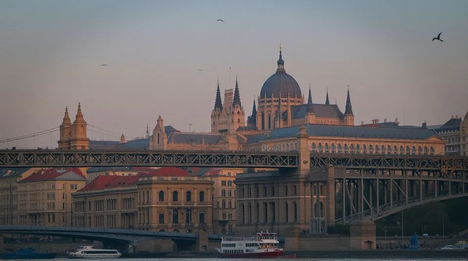 Scenic night view of Budapest’s Parliament Building lit up along the Danube River with Chain Bridge glowing under the evening sky.