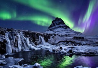 Northern lights dancing over a snow-covered Icelandic mountain and frozen waterfall at night