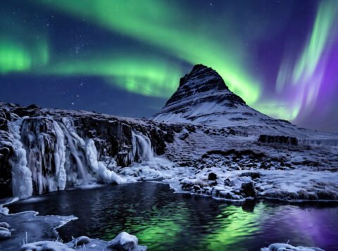 Northern lights dancing over a snow-covered Icelandic mountain and frozen waterfall at night