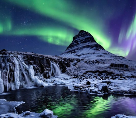 Northern lights dancing over a snow-covered Icelandic mountain and frozen waterfall at night