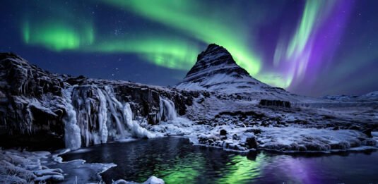 Northern lights dancing over a snow-covered Icelandic mountain and frozen waterfall at night