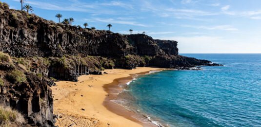 Sunny Canary Islands coastline with volcanic cliffs and golden beach in January