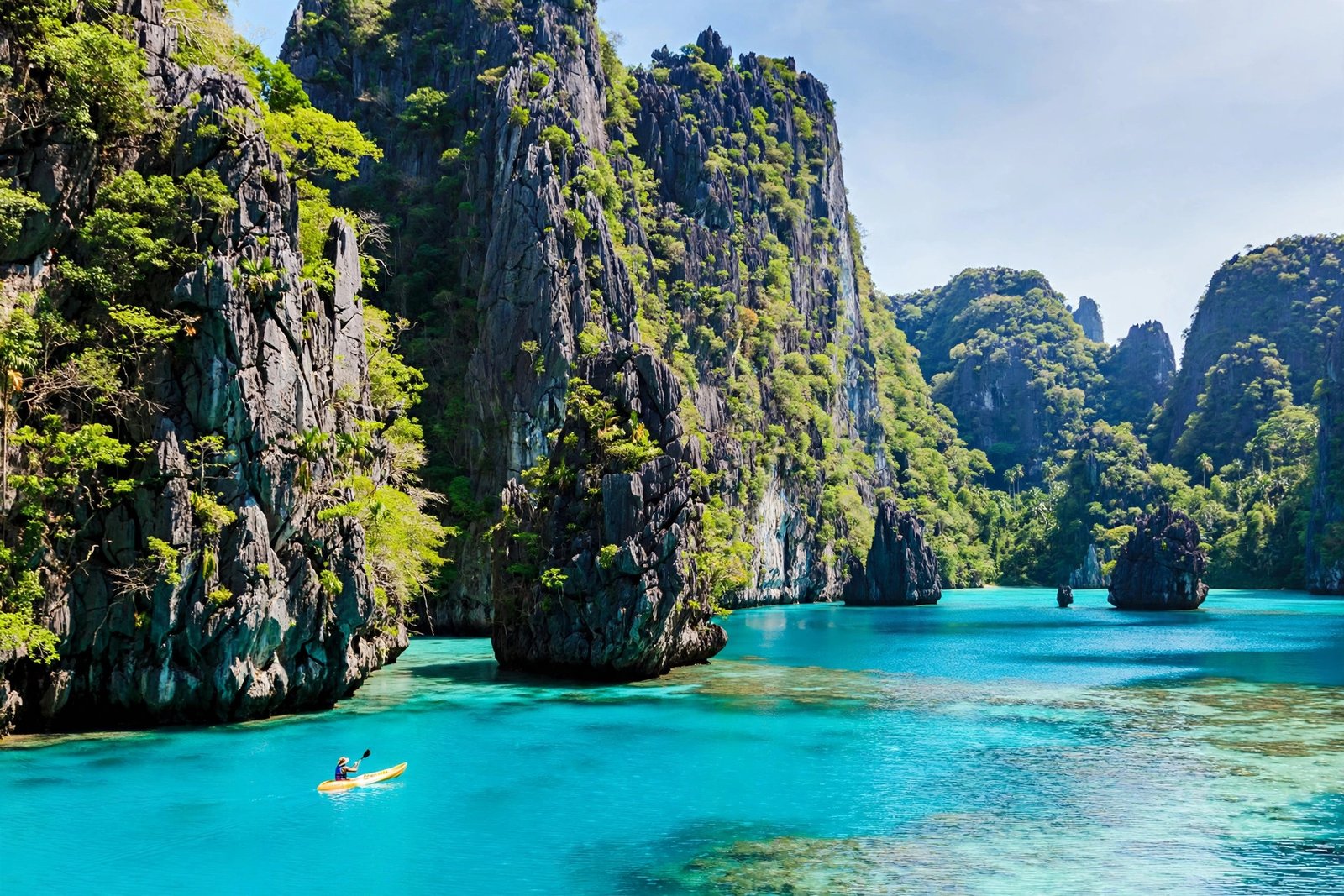Limestone karst cliffs rising from turquoise water in El Nido, Palawan, with a kayaker