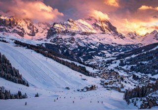 Panoramic golden-hour view of an affordable European ski resort with skiers on snowy slopes