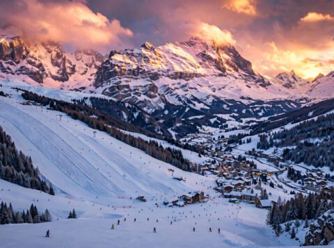 Panoramic golden-hour view of an affordable European ski resort with skiers on snowy slopes
