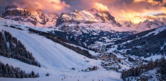 Panoramic golden-hour view of an affordable European ski resort with skiers on snowy slopes